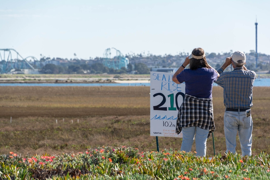 bird watchers at the Kendall-Frost Marsh in front of a sign marking the level of rising seas in year 2100